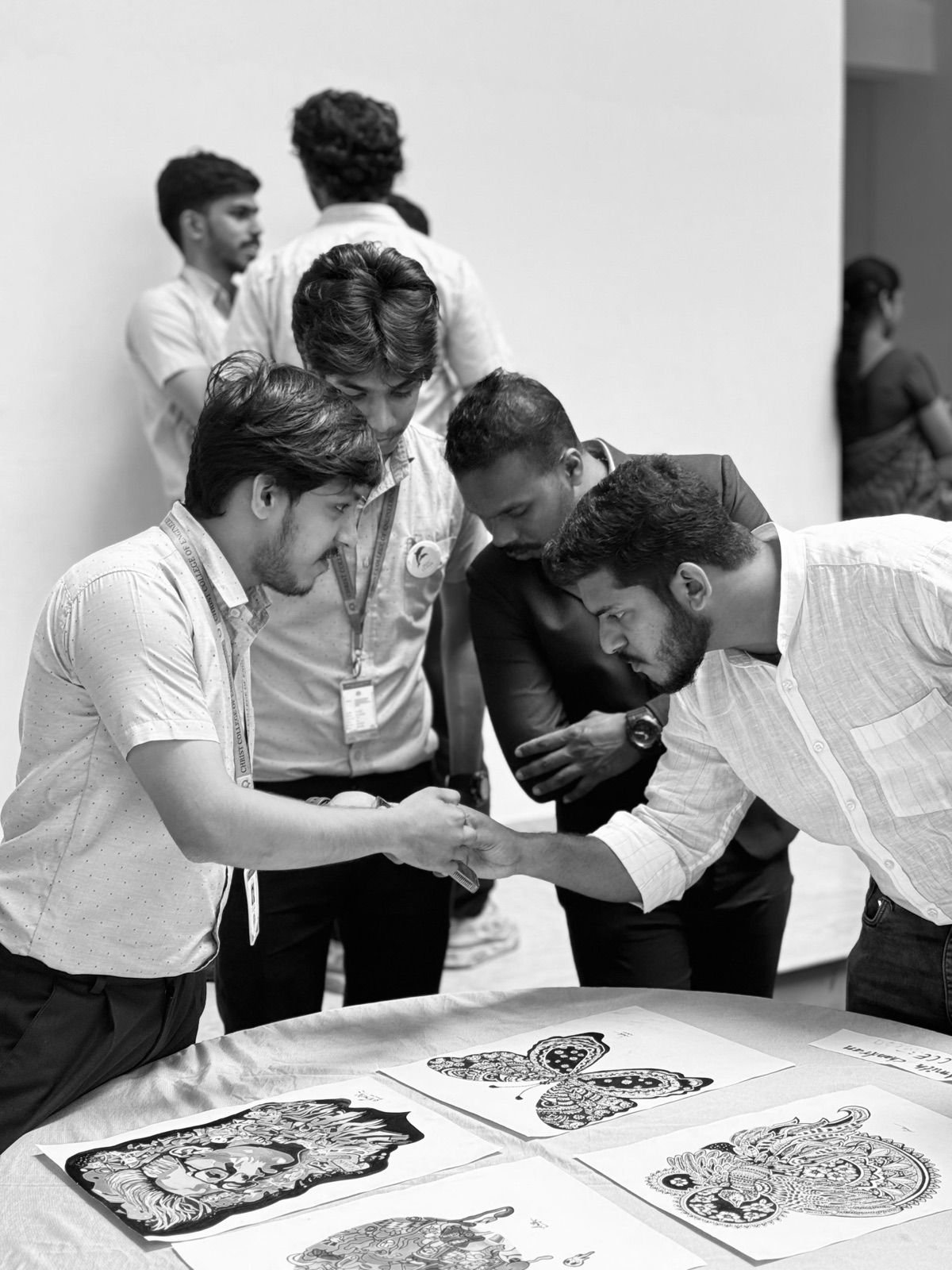 Four people leaning over a table of black-and-white art prints while two of them shake hands.