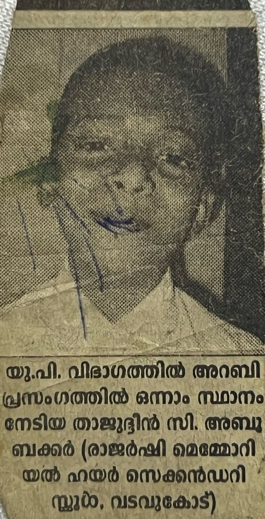 An old, yellowed Malayalam newspaper clipping. A grainy black-and-white photo of a smiling schoolboy sits above a caption saying that Thajudeen C. Abubakkar of Rajarshi Memorial Higher Secondary School, Vadavukode, won first place in Arabic speech in the UP section.