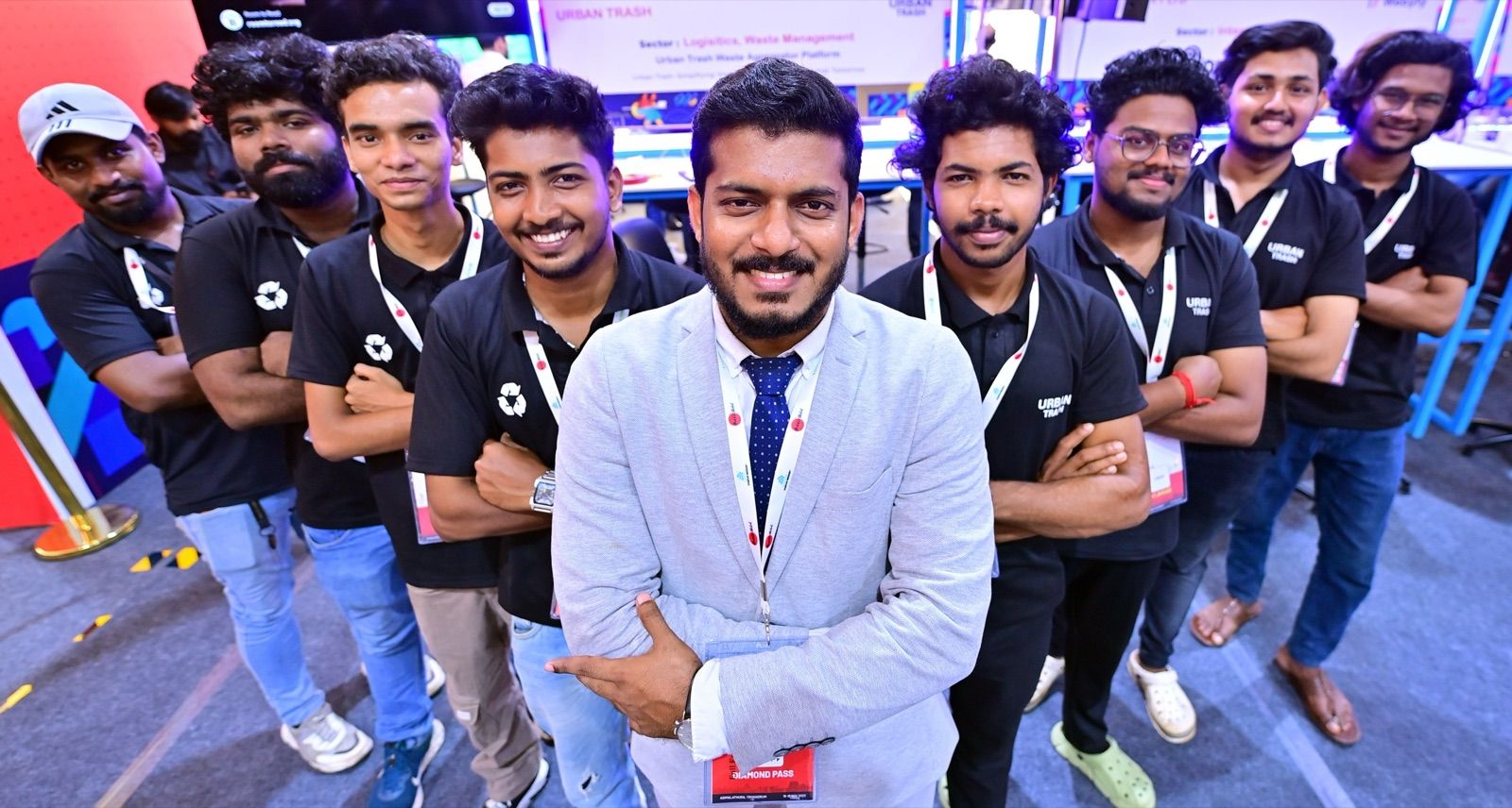 A man in a grey blazer in front of a group of nine people in black shirts and lanyards, at a startup showcase stand.
